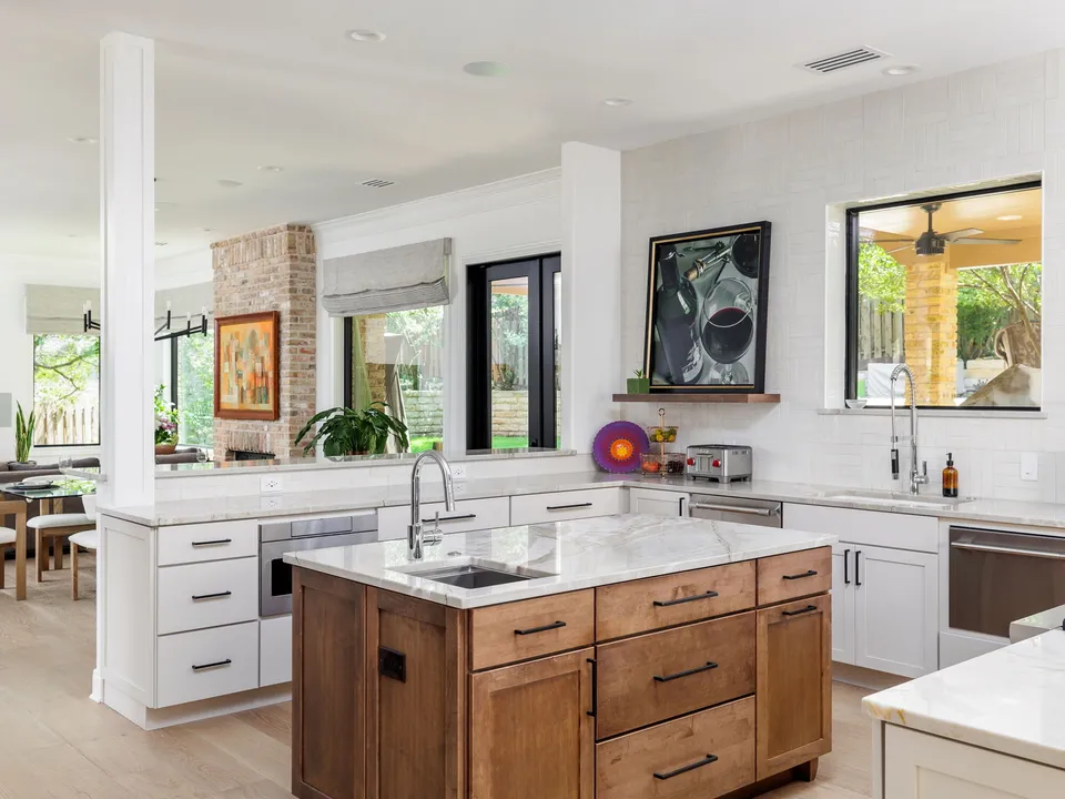 Wood island with a sink and marble top, with a brick column and the living room beyond
