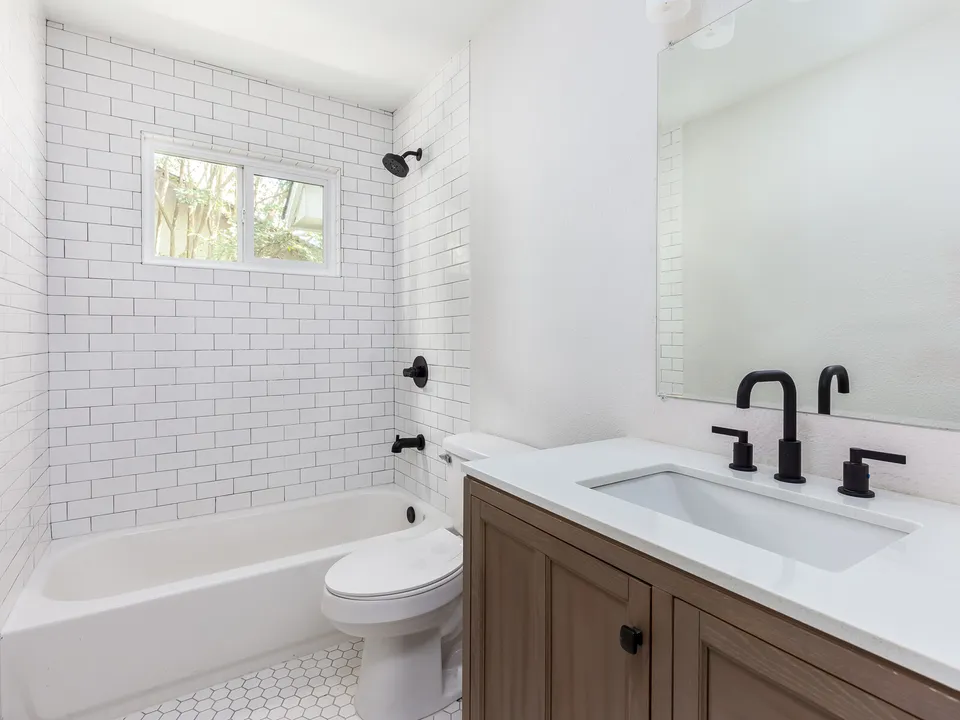 Bathroom with white subway tile, a tub and a walnut vanity with black fixtures
