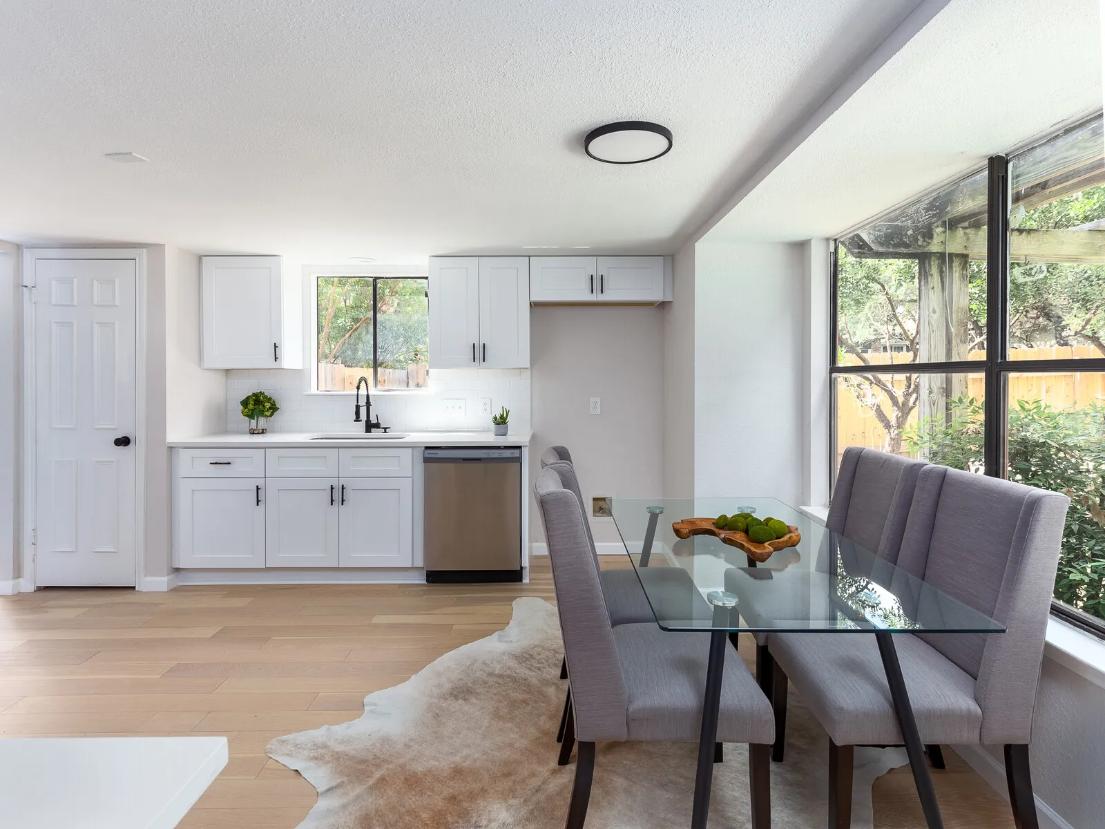 Dining area with a glass table and grey chairs beside a white kitchen