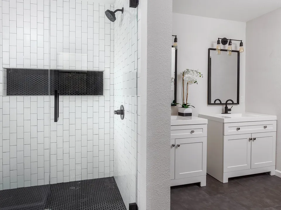 Shower with vertical white tile and a black niche beside two white vanities
