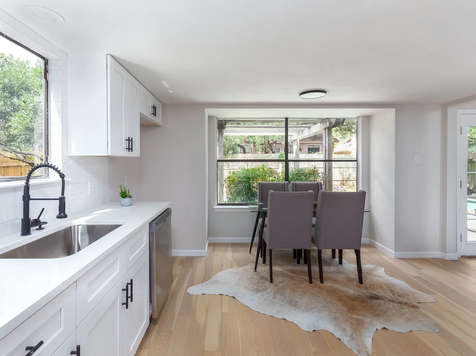 White kitchen sink run with a black faucet looking toward a dining area with a cowhide rug
