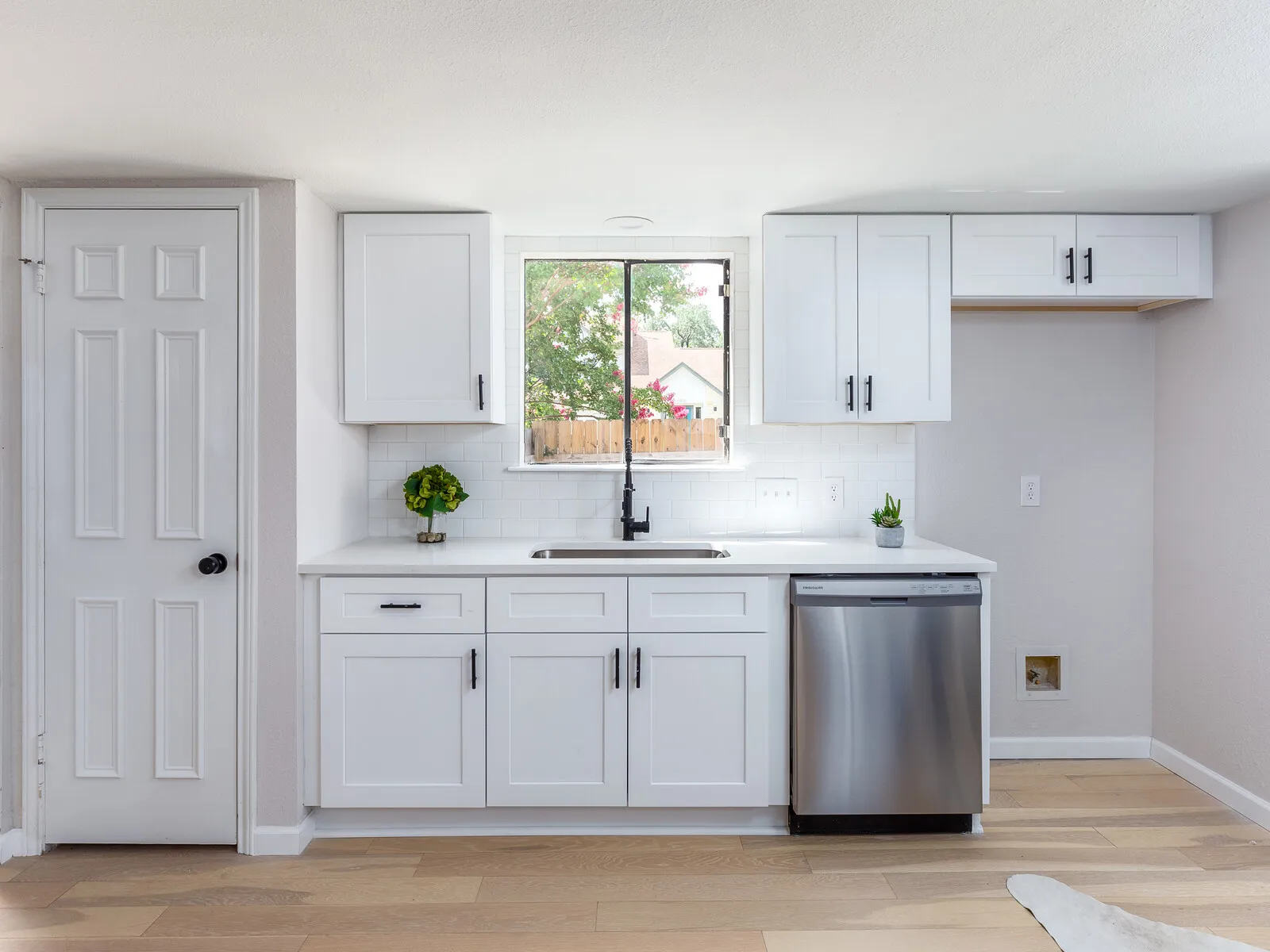 White kitchen sink wall with a window and a stainless dishwasher