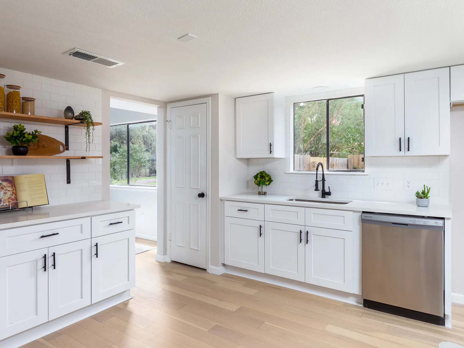 White shaker kitchen with open wood shelves and a stainless dishwasher