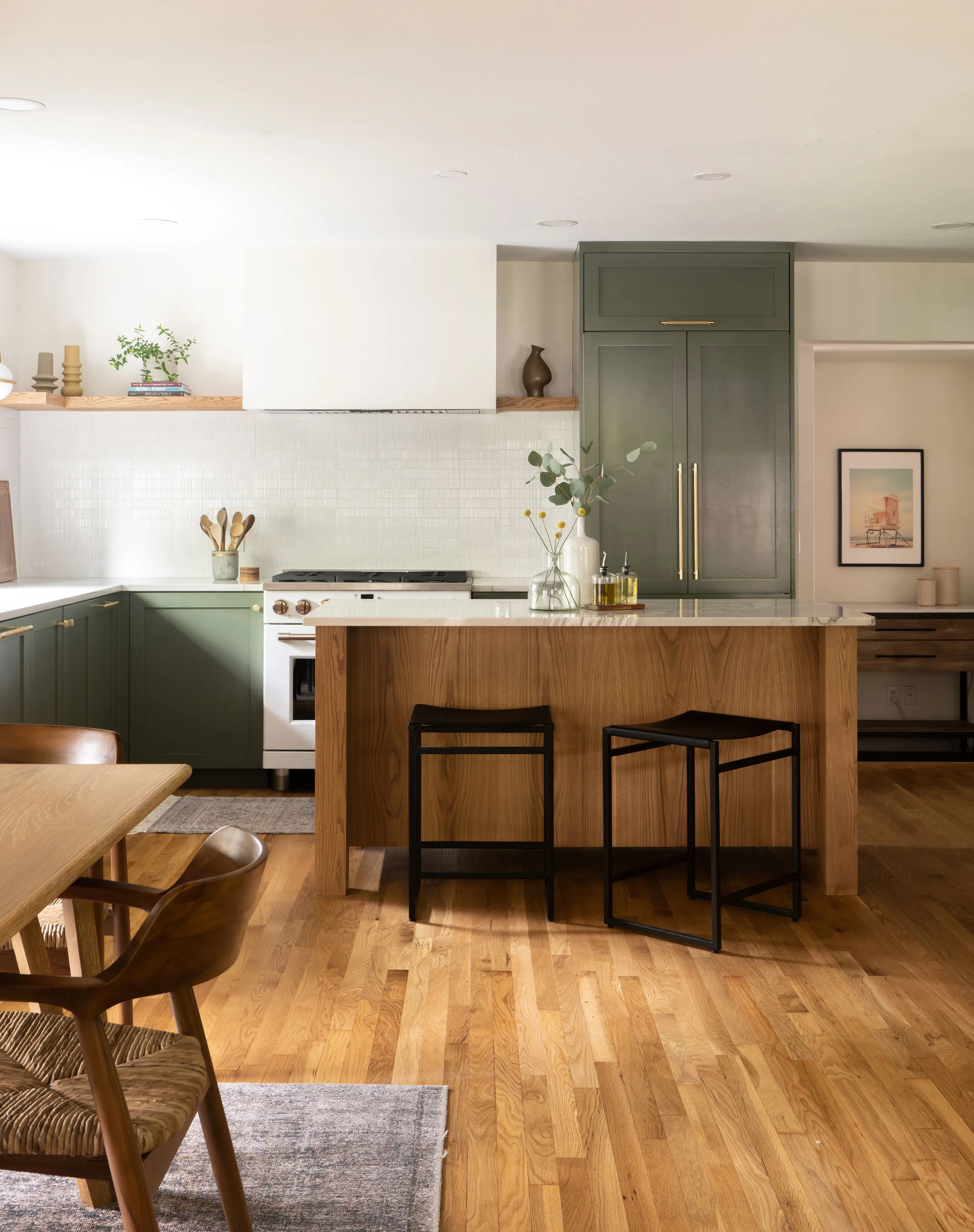 Kitchen with green cabinets, a white oak island with black stools and open wood shelves