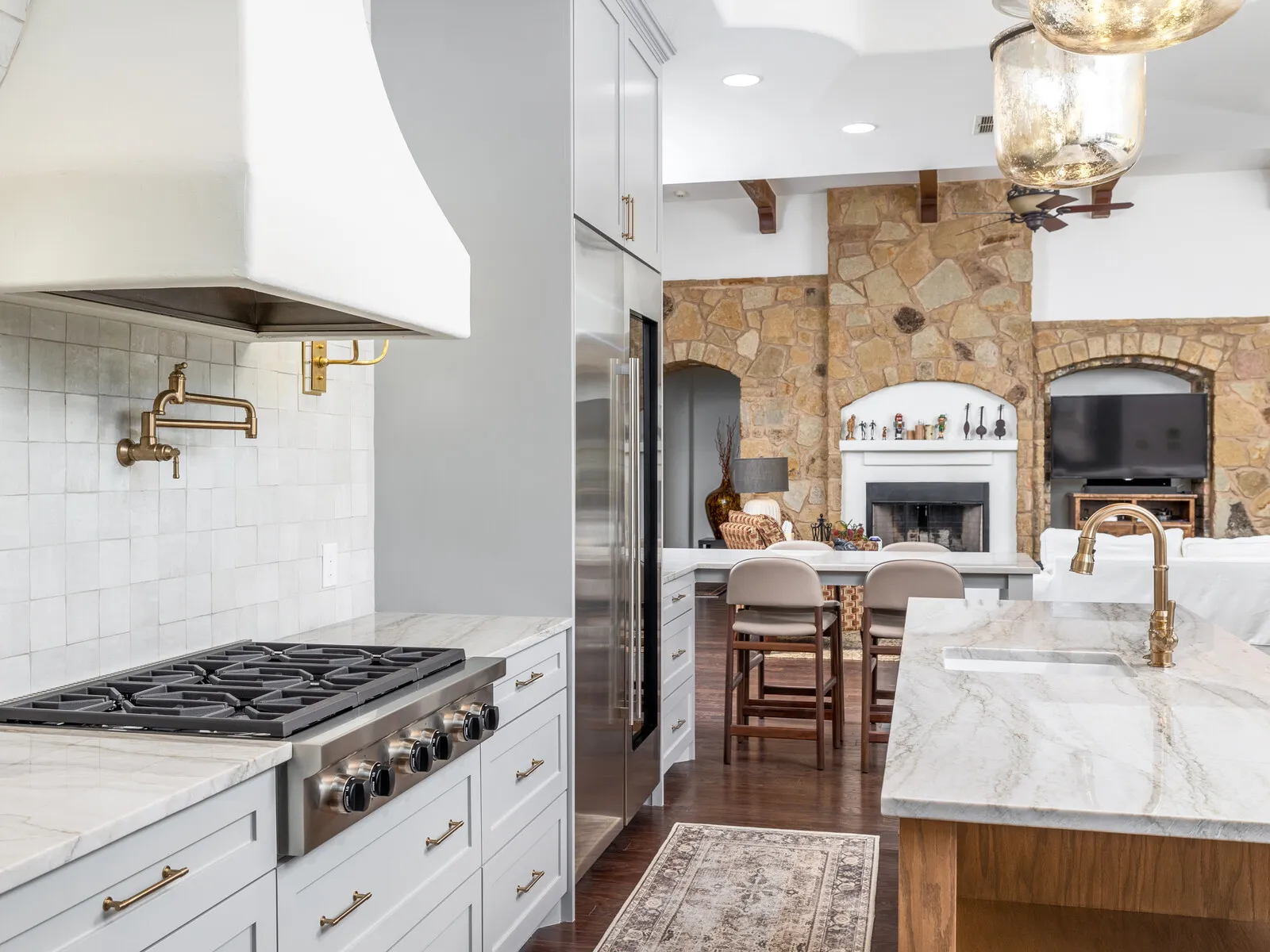 Kitchen with a white plaster range hood, marble counters and a stone fireplace beyond