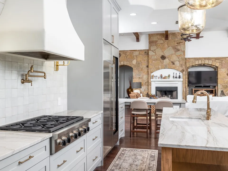 Kitchen with a white plaster range hood, marble counters and a stone fireplace beyond