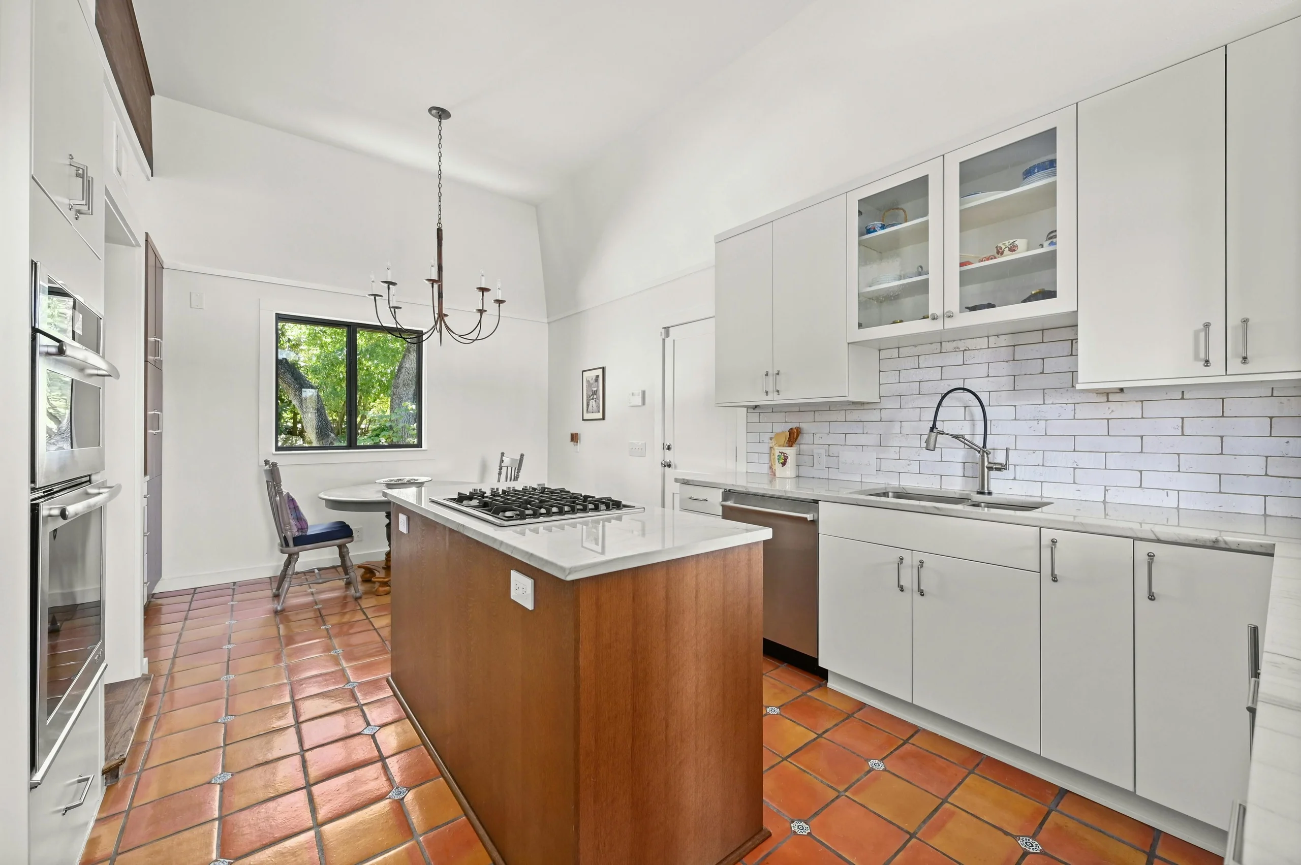 Kitchen with white cabinets, a wood island with a white counter, a chandelier over a dining table and terracotta tile floors