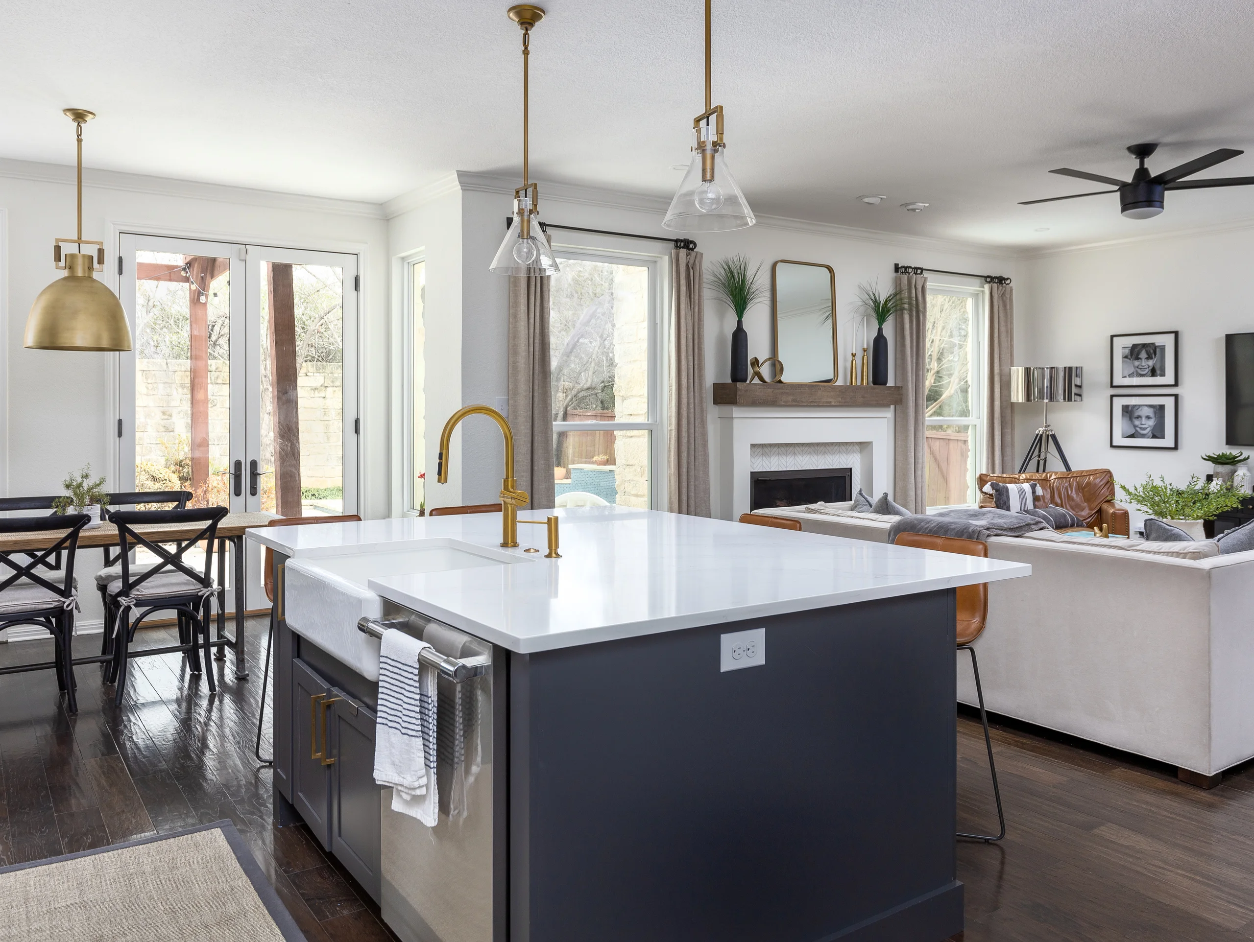 Kitchen with a navy island, farmhouse sink and brass faucet opening to a dining area and living room