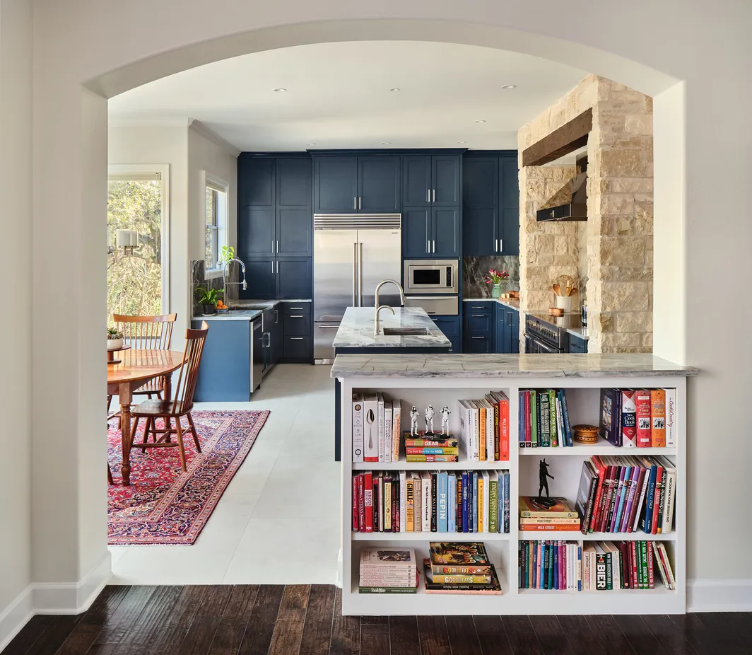 Arched opening with a built-in bookcase looking into a navy kitchen and dining area