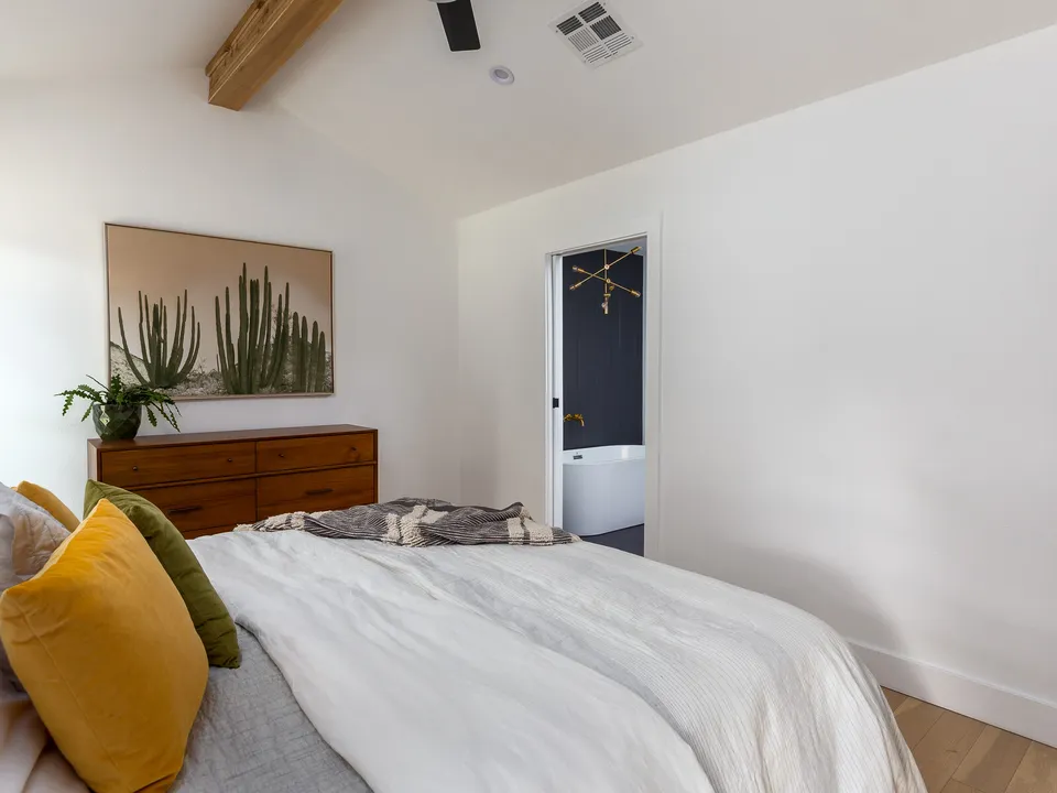 Bedroom with a cactus painting over a mid-century dresser and a doorway to the bath