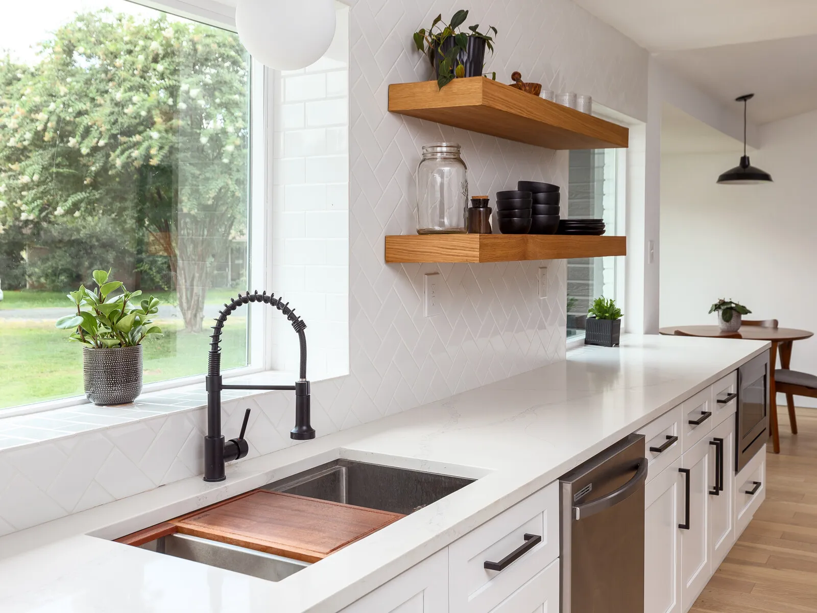 Undermount sink with a black pull-down faucet and a walnut cutting board below walnut floating shelves