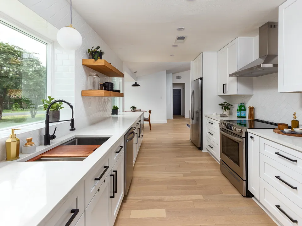 Galley kitchen with white shaker cabinets, a copper sink insert and walnut shelves