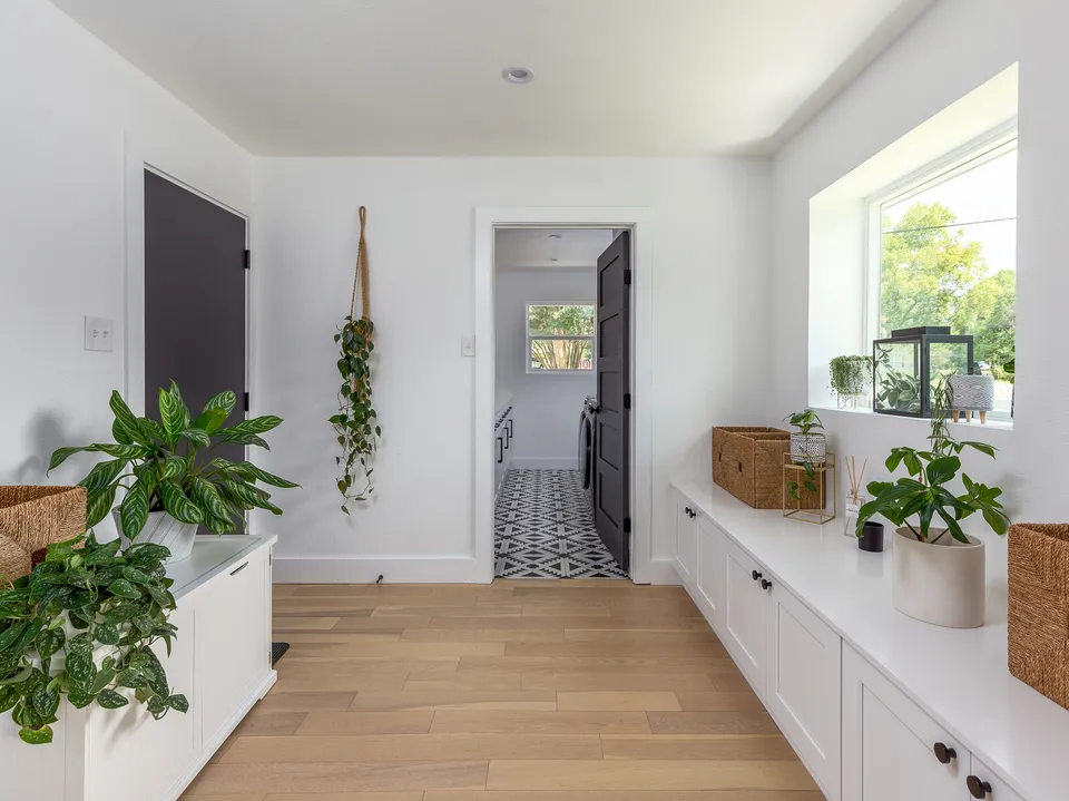 Hallway with white built-in cabinets, plants and a view into the laundry room