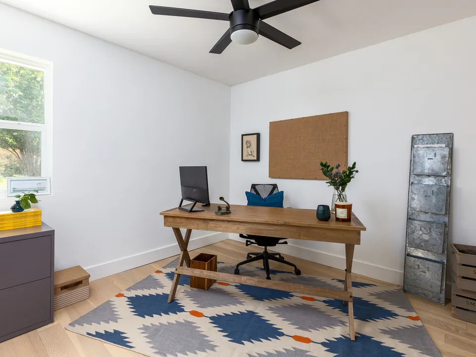 Home office with a wood desk, a cork board and a blue patterned rug