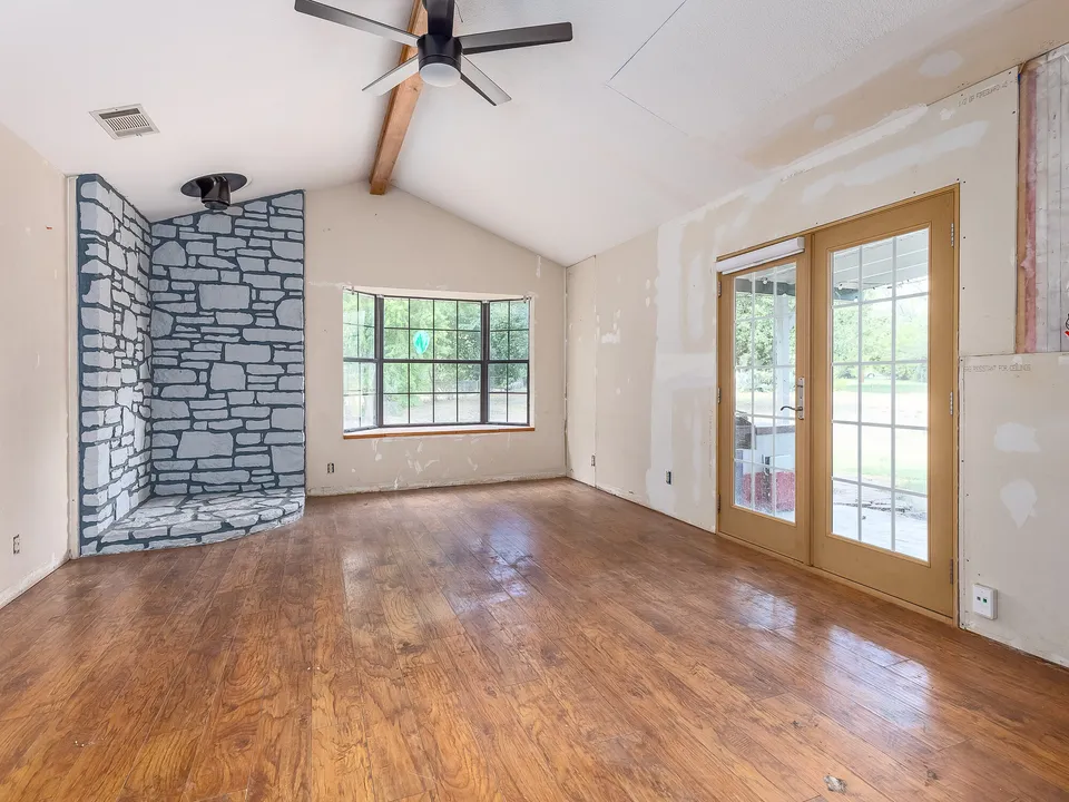 Living room before the remodel, with a stone fireplace wall, worn wood floors and bare drywall