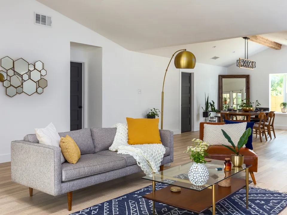 Living room with a grey sofa and a brass arc lamp, open to the dining area