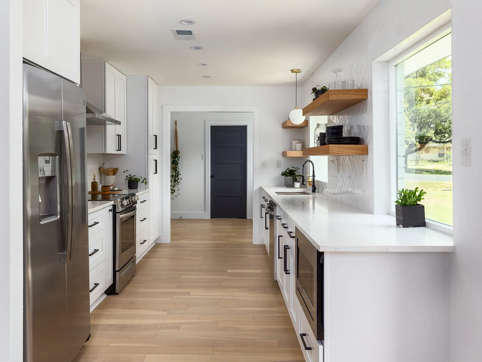 Long galley kitchen with white shaker cabinets, a stainless refrigerator and light wood floors