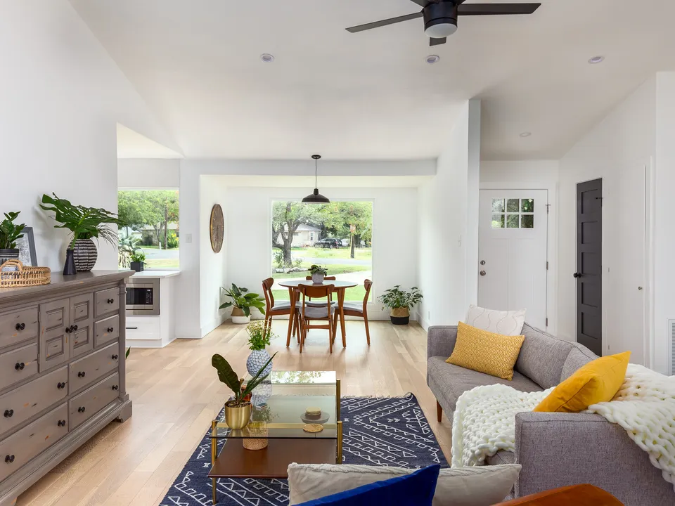 Open living room with a grey sofa, a blue rug and a dining area by a large window