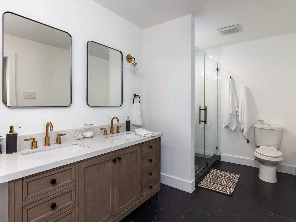 Primary bath with a wood double vanity, black mirrors and a glass shower