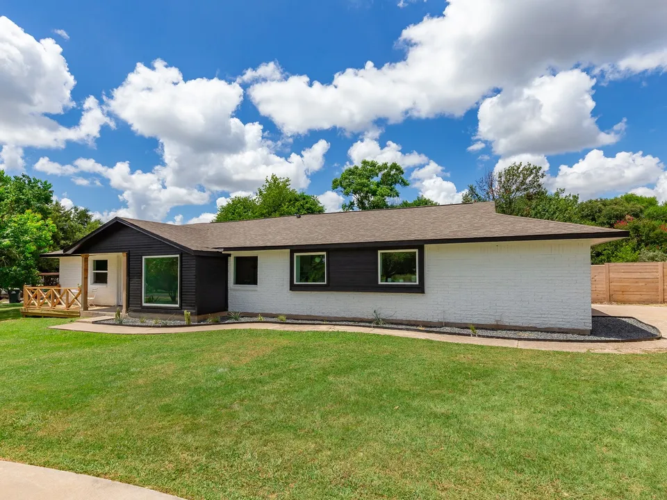 Ranch house with white brick, navy siding and a cedar porch railing behind a green lawn