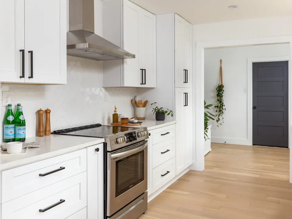 Stainless range with a chimney hood and white tile, looking toward a black interior door