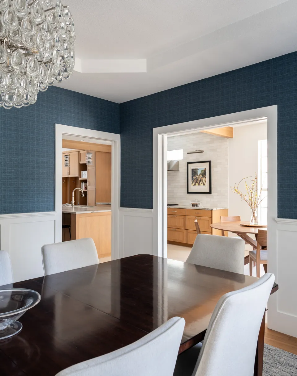 Dining room with navy grasscloth walls, white wainscoting and a crystal chandelier