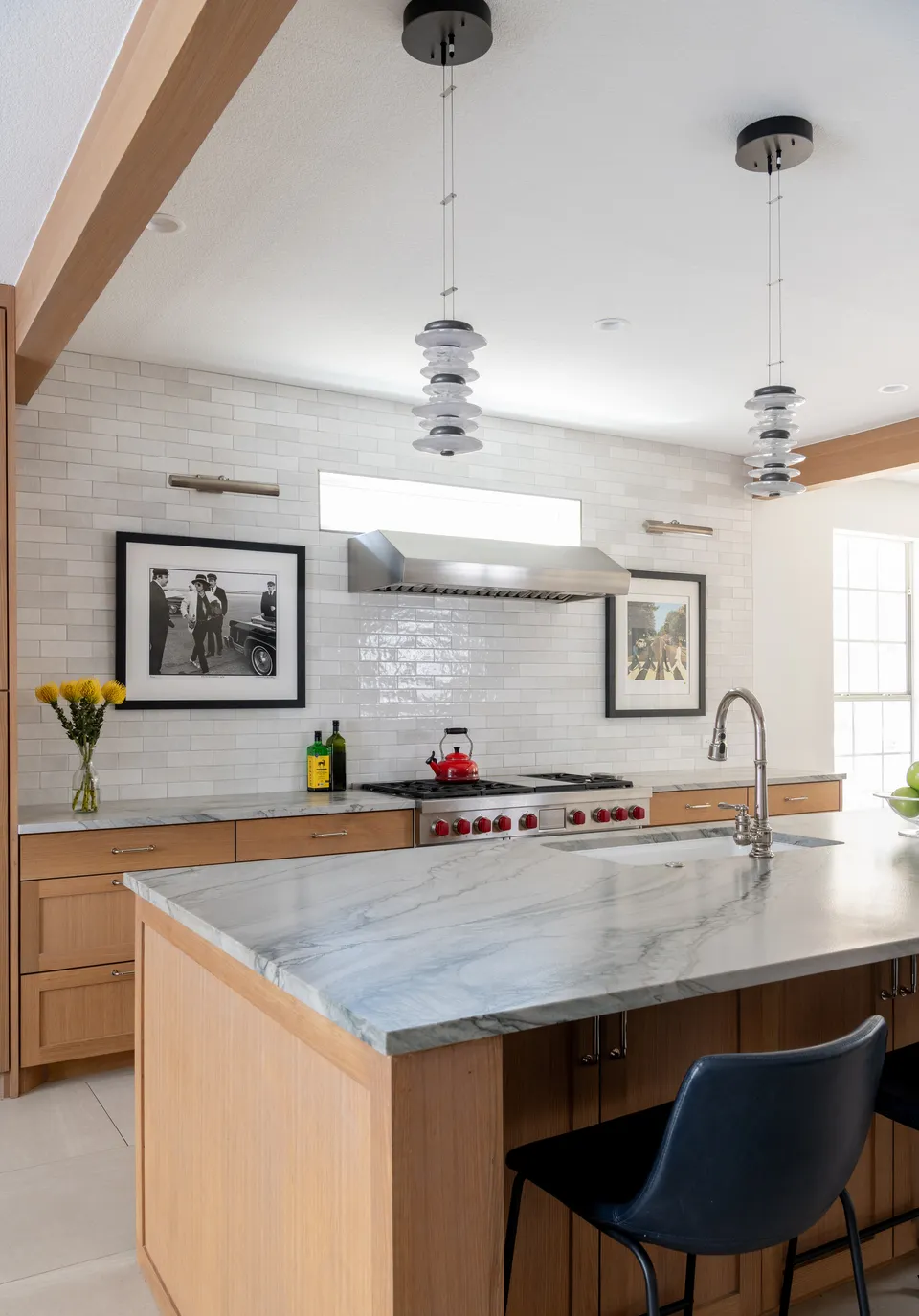 Marble island with navy bar stools in front of the range wall and glass pendants