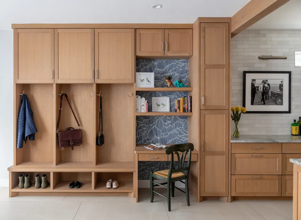 Mudroom with white oak cubbies and coat hooks beside a built-in desk and bookshelves