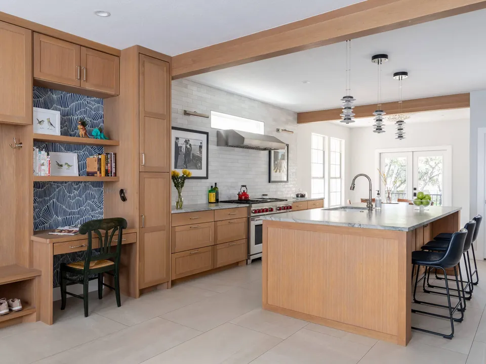 Open kitchen with white oak cabinets, a desk nook and a marble island with navy bar stools