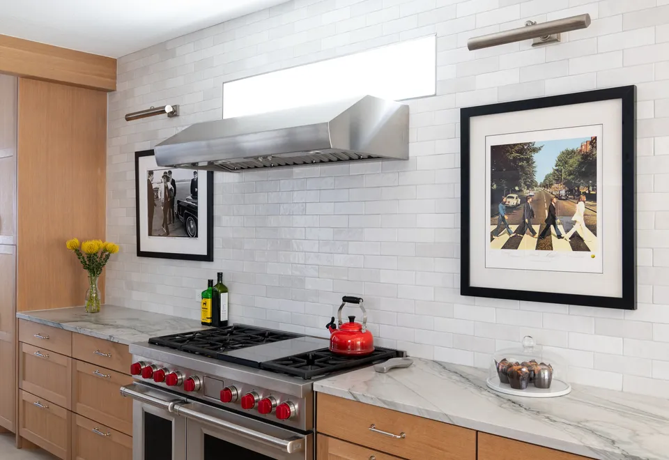 Range wall with white glazed tile, a stainless hood, a red-knob range and framed prints