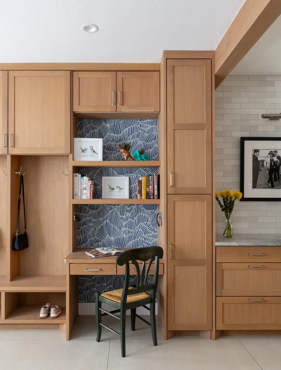 White oak cabinets around a desk nook with blue patterned wallpaper and open shelves