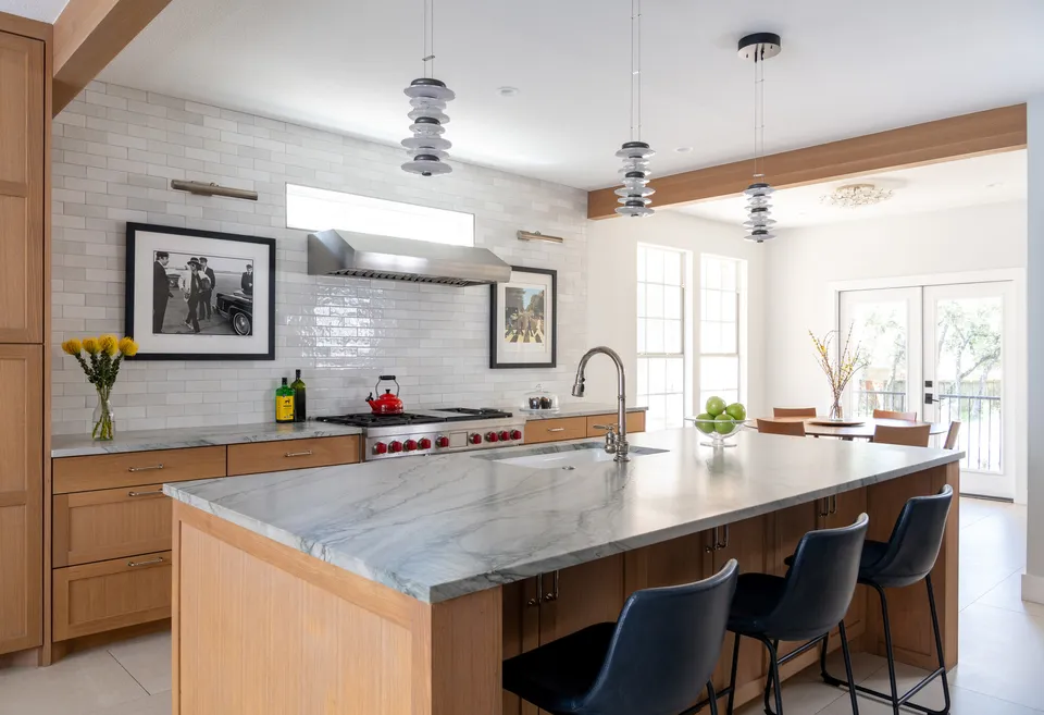 White oak kitchen island with a marble top and navy leather bar stools