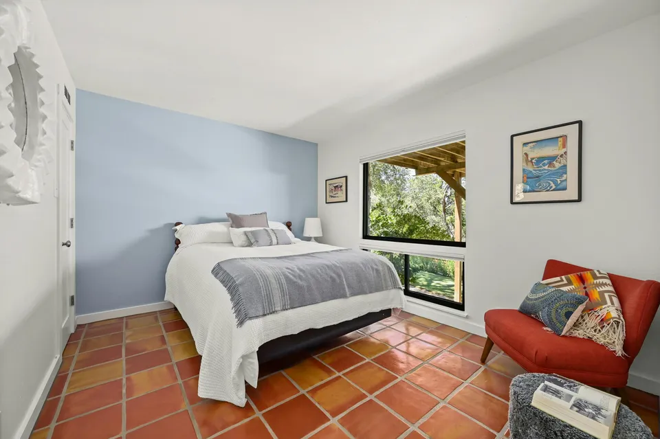 Bedroom with a blue accent wall, Saltillo tile and a red chair