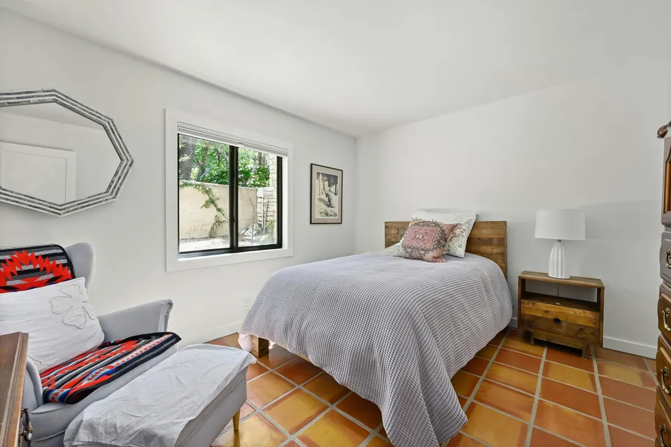Bedroom with Saltillo tile, a wood bed and a grey armchair