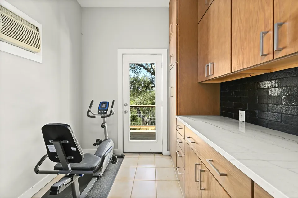 Casita gym with wood cabinets, a black tile backsplash and an exercise bike