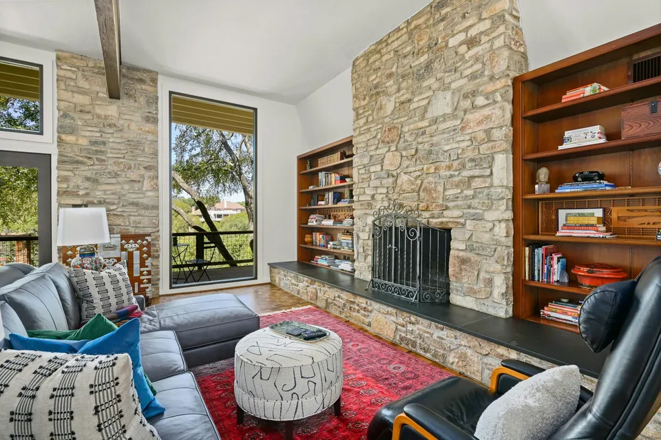 Den with a stone fireplace, built-in wood bookshelves and a red rug
