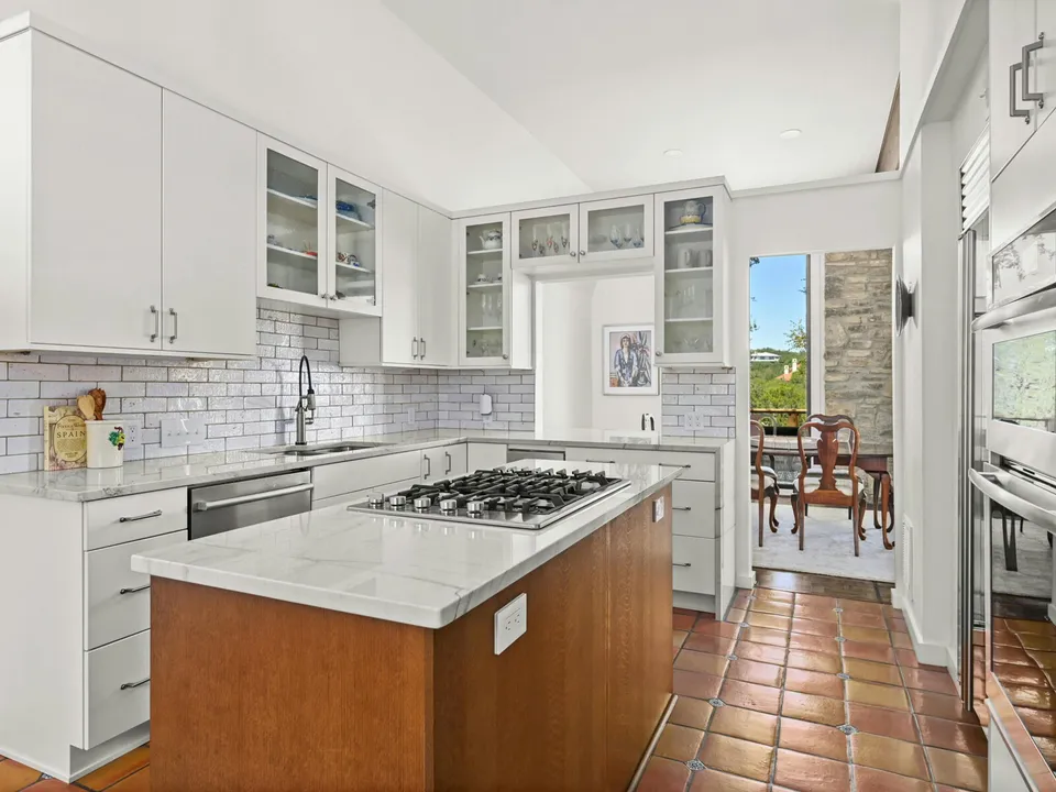 Kitchen with white cabinets, a wood island with a cooktop and Saltillo tile floors