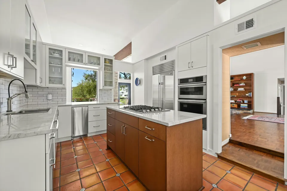 Kitchen after the remodel, with white cabinets, a wood island with a cooktop and Saltillo tile floors