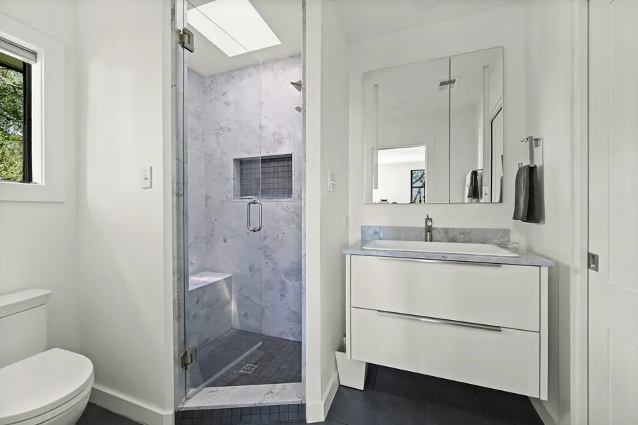 Primary bath with a marble shower, a skylight and a white floating vanity