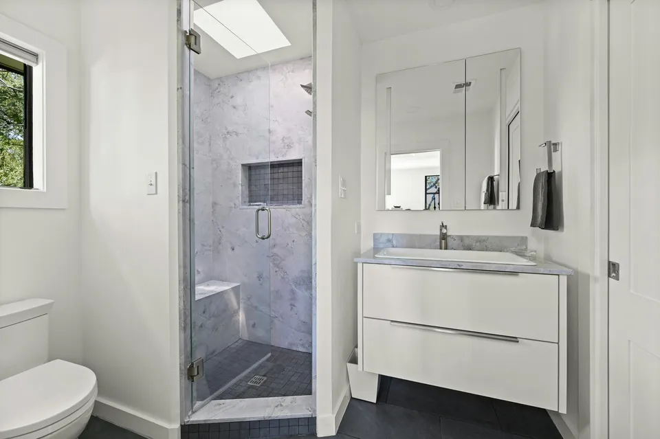 Primary bath with a marble shower, a skylight and a white floating vanity