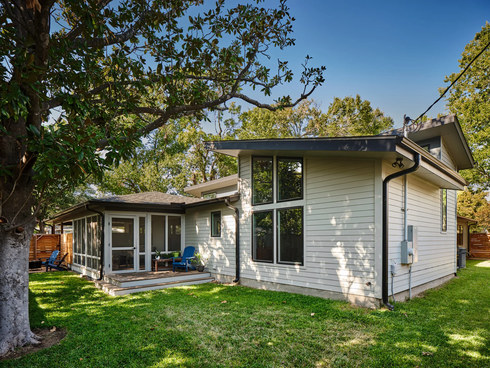 Back of a house with an added screened porch and a wing with tall windows, under a large oak tree