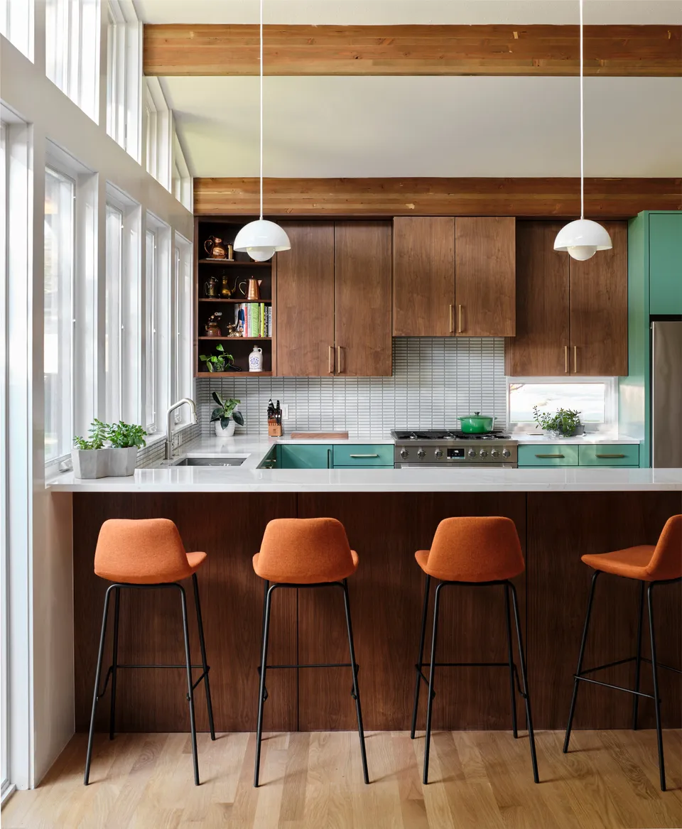 Walnut peninsula with orange bar stools below tall windows and white globe pendants