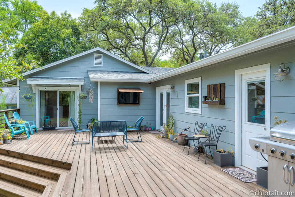 Back deck with blue chairs and a grill beside the blue-grey house