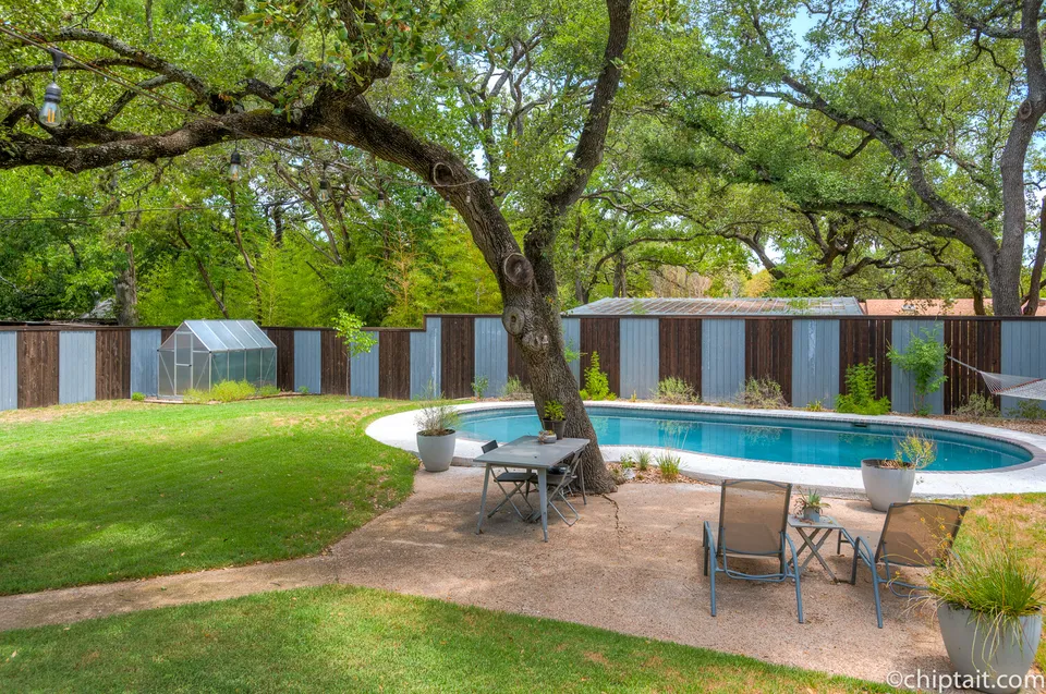 Backyard with a pool under a large oak and a corrugated metal fence