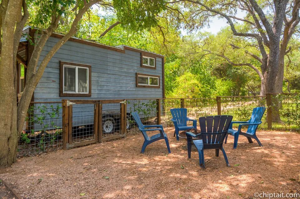 Fire pit with blue Adirondack chairs beside a tiny house