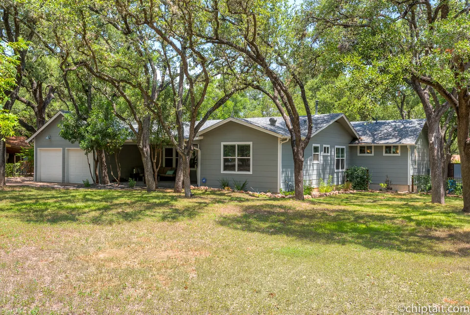 Front yard with oak trees and the blue-grey house beyond