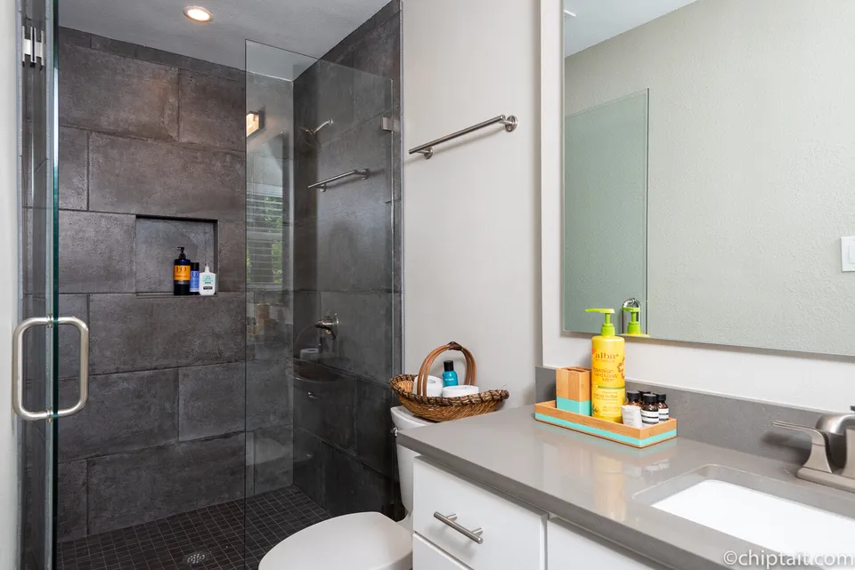 Glass shower with dark slate tile beside a grey quartz counter