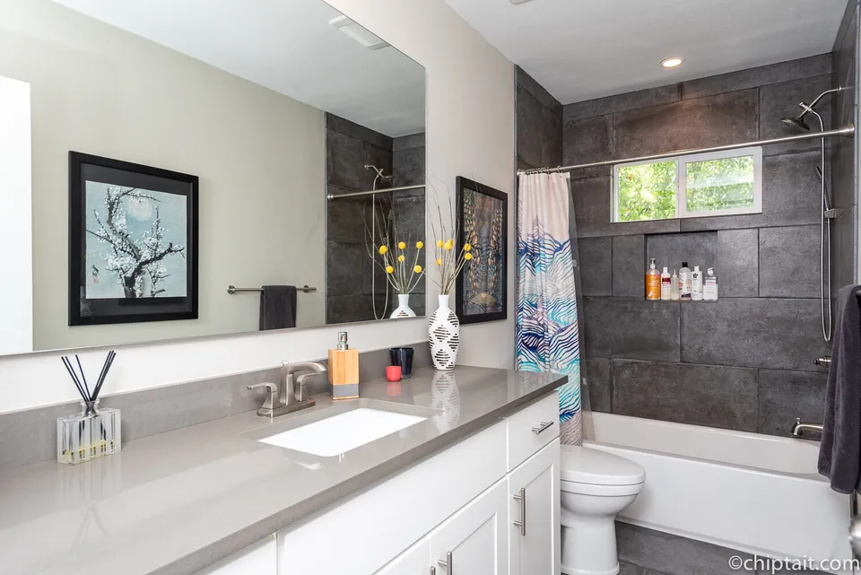 Hall bath with a grey quartz vanity and a tub with dark slate tile