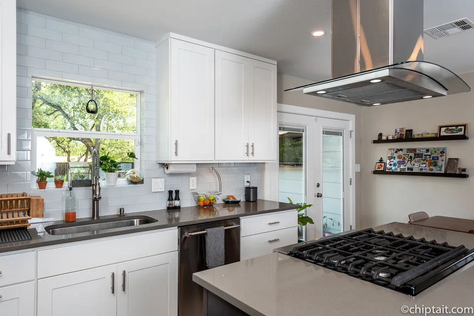 Kitchen with a gas cooktop island, a stainless hood and a window over the sink