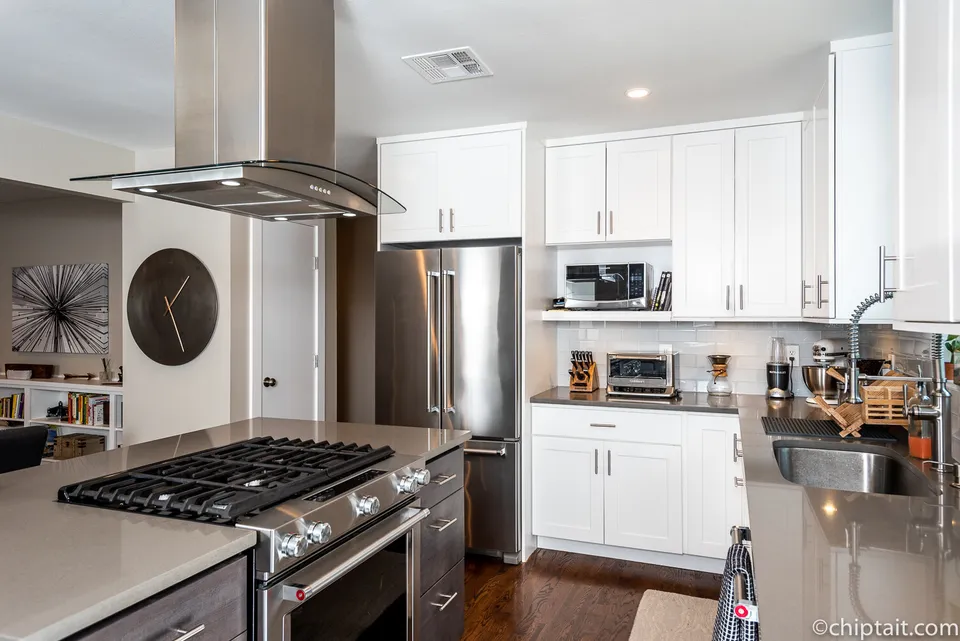 Kitchen with a stainless range on the island, a chimney hood and white cabinets